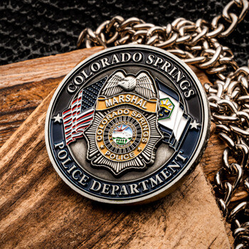 Colorado Springs Police Department challenge coin featuring a Marshal badge emblem flanked by American and Colorado flags on a wooden surface.