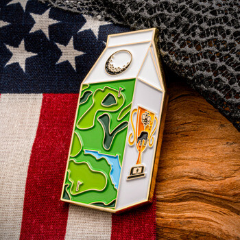 Milk carton shaped challenge coin with a green golf course design and a golf trophy graphic, set against an American flag and textured fabric.