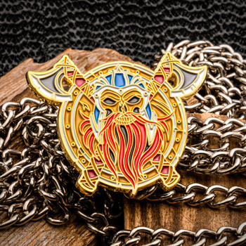 Gold plated Viking warrior lapel pin featuring a detailed bearded face, helmet, and crossed battle axes set against a metal chain and wooden background.