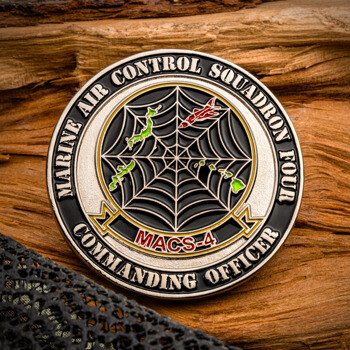 Marine Air Control Squadron Four MACS-4 Commanding Officer challenge coin displaying a spiderweb design, map outlines, and a jet against a wooden background.
