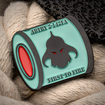 A barrel-shaped military challenge coin for ABTRY 2-142FA with a black helmet design, light blue enamel, and red accents, placed on a thick white rope.