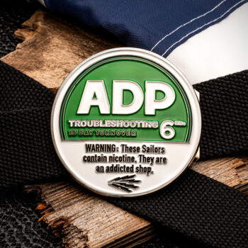 ADP Troubleshooting challenge coin with green and white design resembles a tobacco can, set against an American flag and black belt background.