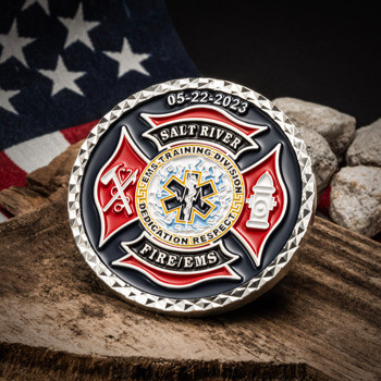 Salt River Fire EMS challenge coin featuring a Maltese cross, Star of Life, and diamond cut edge displayed on a wooden block with rocks and an American flag.