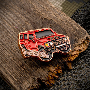 Custom lapel pin shaped like a red off-road vehicle with the inscription Together We Can Conquer the Impossible on a wooden surface.
