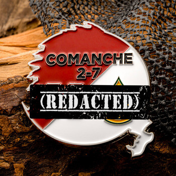 Red and white circular custom challenge coin featuring the text COMANCHE 2-7, resting on a textured wooden background.