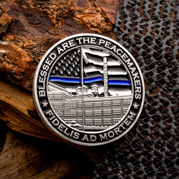 Circular challenge coin featuring a thin blue line American flag design and the text Blessed Are The Peacemakers Fidelis Ad Mortem, resting on textured bark.
