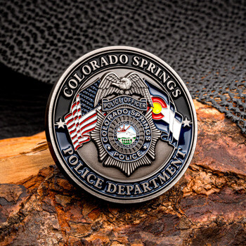 Colorado Springs Police Department challenge coin featuring a central officer badge, US flag, and Colorado state flag, resting on a textured wooden background.