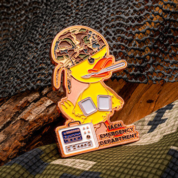 Yellow rubber duck lapel pin dressed in military combat gear with a camouflage helmet, thermometer, and cardiac monitor, labeled IACH Emergency Department.