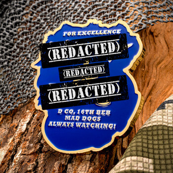 Shield-shaped blue and gold challenge coin featuring redacted text bars and D Co 16th BEB Mad Dogs inscription on a rustic camo background.