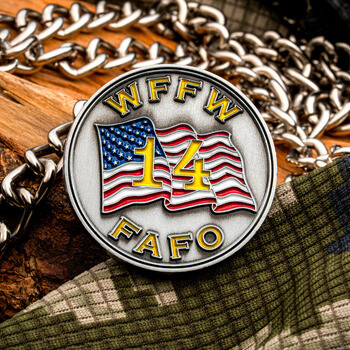 Silver challenge coin with an American flag, number 14, and the text WFFW and FAFO on camouflage fabric with a chain.
