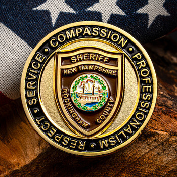 Rockingham County Sheriff New Hampshire gold challenge coin resting on wood against an American flag.