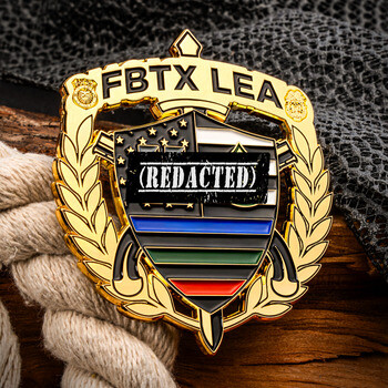 Gold shield challenge coin with FBTX LEA lettering, laurel wreath, and thin line flag emblem displayed on wood and rope.