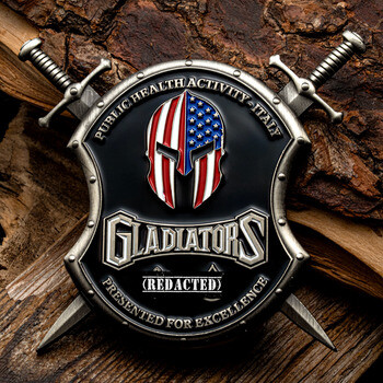 Shield-shaped challenge coin with crossed swords, American flag Spartan helmet, and Gladiators text for Public Health Activity Italy.