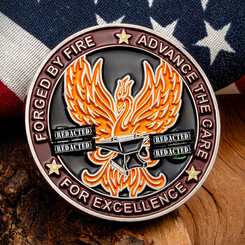 Challenge coin featuring an orange phoenix and anvil emblem with the text Forged By Fire, Advance The Care, and For Excellence against an American flag.