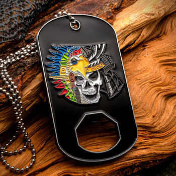 Black dog tag bottle opener challenge coin with ball chain featuring an Aztec eagle warrior skull emblem against a natural wood backdrop.