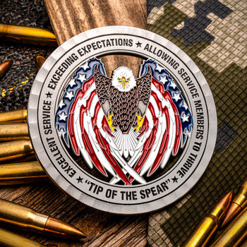 Tip of the Spear military challenge coin featuring an eagle with American flag wings, displayed with rifle ammunition on camouflage cloth.