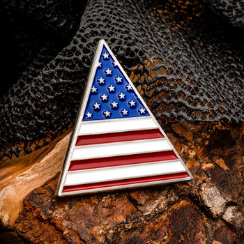 Triangular folded American flag lapel pin on camouflage fabric and wood backdrop.