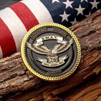 Anaheim Police SWAT gold challenge coin featuring an eagle emblem, displayed on a wooden log in front of an American flag.
