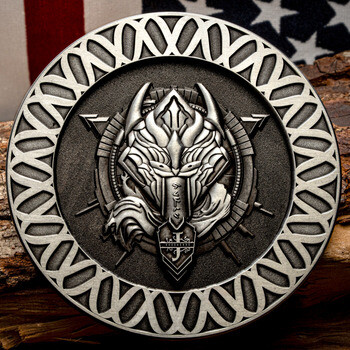 Antiqued silver challenge coin featuring an armored wolf head emblem and Celtic knot border, resting on wood against an American flag.