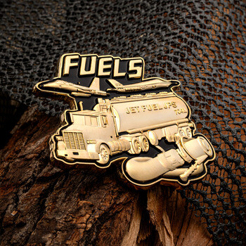 Gold lapel pin featuring FUELS text with an aircraft refueling truck, plane, and hose nozzle against a dark background.