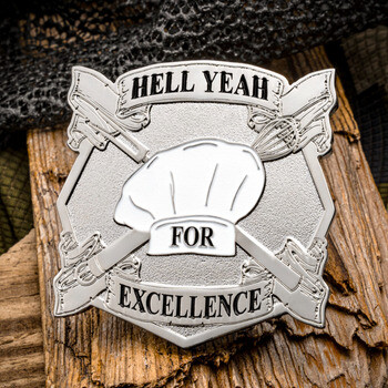 Shield-shaped silver challenge coin featuring a chef hat, crossed spatula and whisk, with banners reading Hell Yeah for Excellence.
