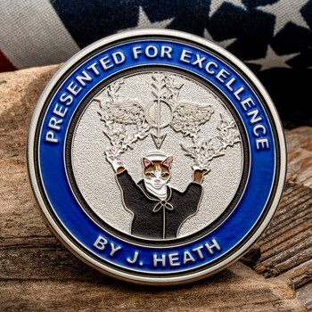 Silver and blue challenge coin inscribed Presented for Excellence By J. Heath, featuring an illustrated cat figure.